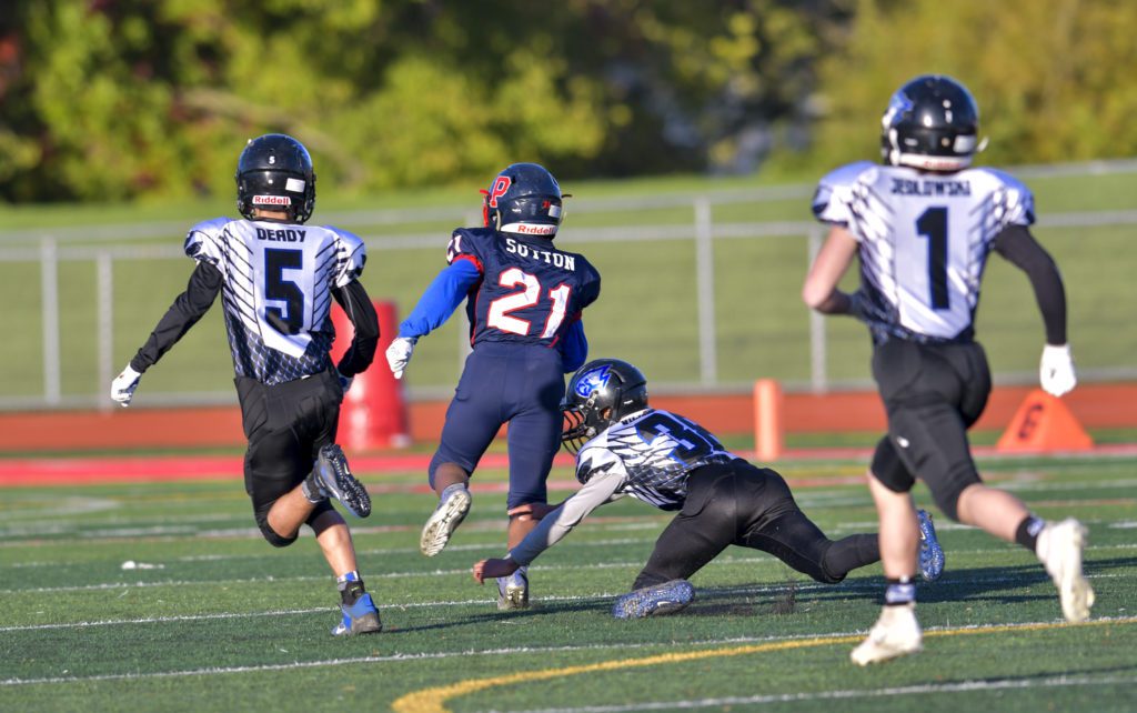 American football players running down field during game.